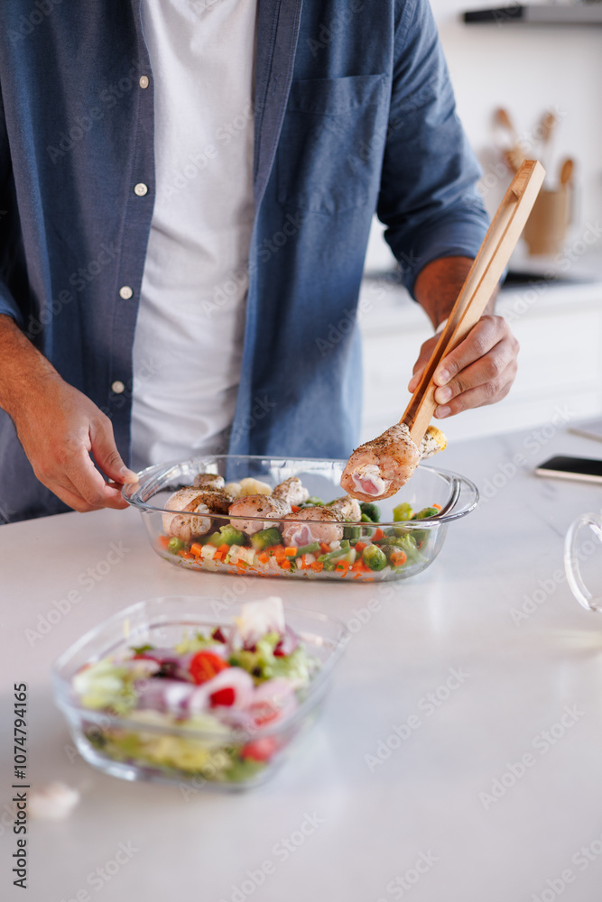 Partial view of black man putting raw chicken in baking dish with vegetables near blurred salad in kitchen Partial view of black man putting raw chicken in baking dish with vegetables near blurred salad in kitchen