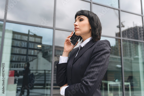 Businesswoman speaking on the phone outdoors in front of a modern building during an overcast day