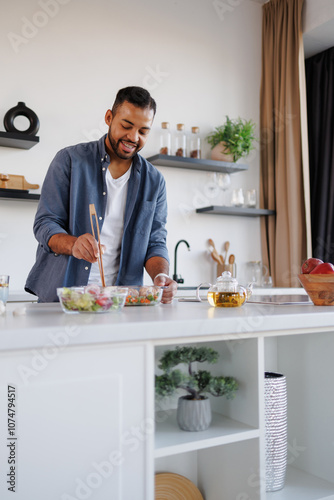 Young african american man cooking dinner near fresh salad and herbal tea in kitchen