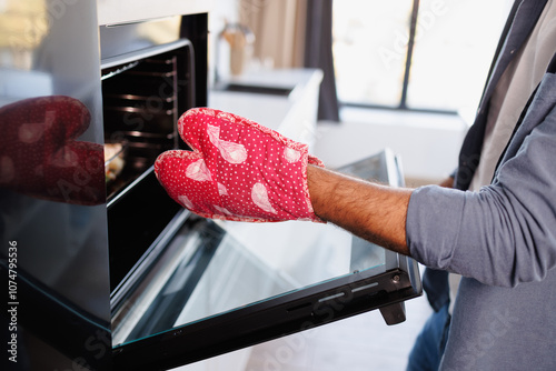 Partial shot of african american man in glove opening oven while preparing food at home photo