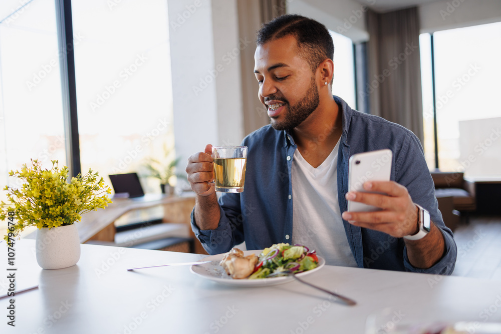 African american man holding cup of tea and smartphone near fresh lunch at home African american man holding cup of tea and smartphone near fresh lunch at home
