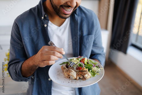 Partial shot of smiling african american man having chicken and salad for lunch at home