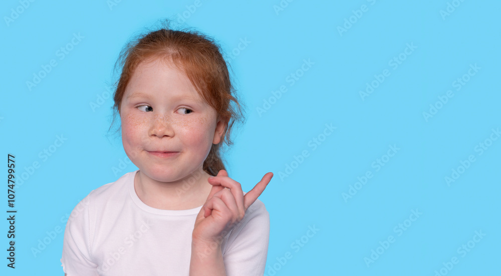 A smiling girl with red hair playfully pointing to the side against a bright blue background during a cheerful moment A smiling girl with red hair playfully pointing to the side against a bright blue background during a cheerful moment