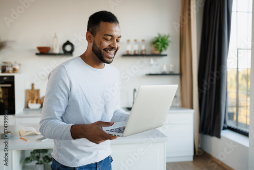 Cheerful african american man using laptop in kitchen at home