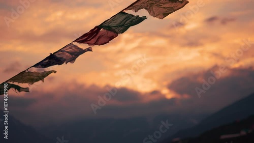4K Slow motion shot of prayer flags waving in the wind in front of snowy Himalayan mountain peaks covered by clouds during the sunset at Khangsar village in Lahaul valley, Himachal Pradesh, India.	