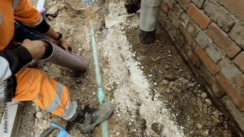 Worker installing a telecom duct fro internet broadband cable  alongside a brick wall in a construction site during the day