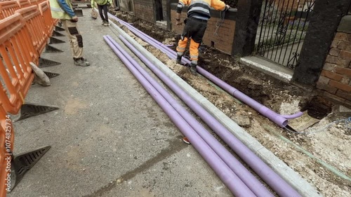 Worker installing a telecom duct fro internet broadband cable  alongside a brick wall in a construction site during the day