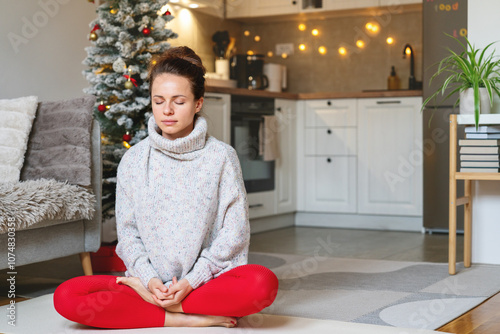 Serene woman in half lotus pose meditating at home during Christmas holidays, embracing self-care and winter harmony. photo