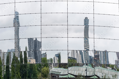 A panoramic reflection of an impressive city skyline captured in a large mirrored surface, evoking themes of urban complexity and the beauty of architectural symmetry.