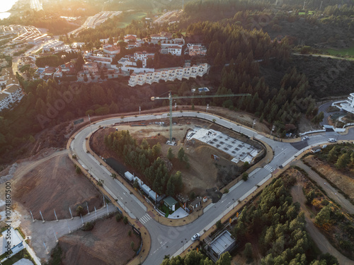 Aerial view of a construction site near the coast with residential buildings, green spaces, and roads