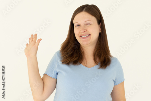 Cheerful friendly girl saying hello, winking and smiling, waving hand at camera, say hi and greet you, standing against white background