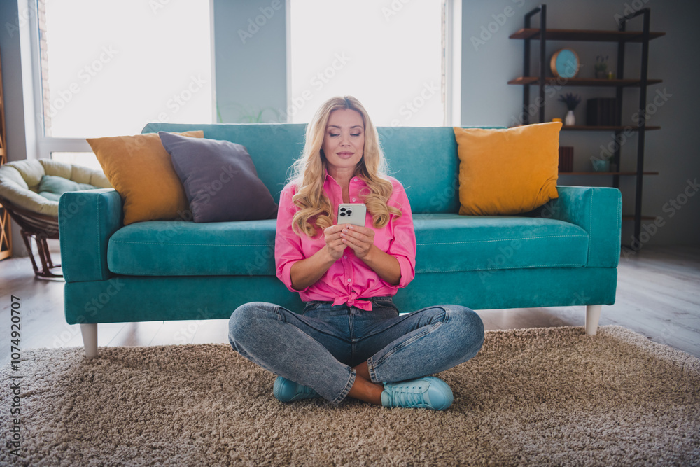 Young woman enjoying leisure time at home, sitting comfortably on carpet with smartphone in a cozy living room setting. Young woman enjoying leisure time at home, sitting comfortably on carpet with smartphone in a cozy living room setting.