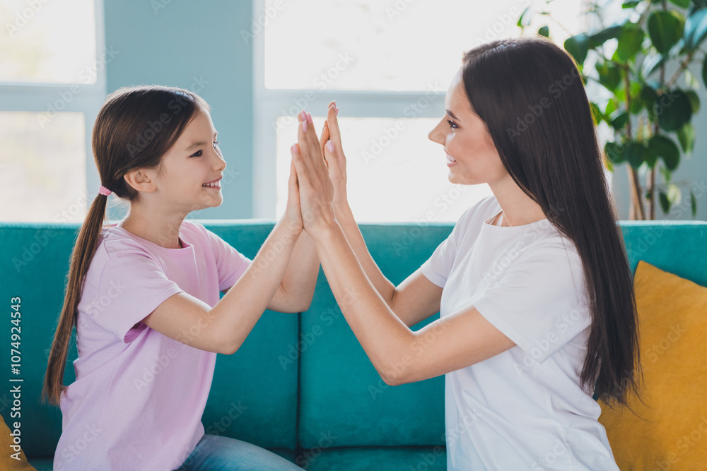 Lovely positive charming mum and her nice small daughter sitting on sofa clapping palms indoors Lovely positive charming mum and her nice small daughter sitting on sofa clapping palms indoors