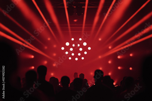 Silhouettes of people in a dark room illuminated by red lights and beams creating an energetic concert or club atmosphere 