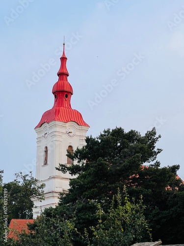 Historic church tower with red spire surrounded by lush greenery in Modrice, Czech Republic.