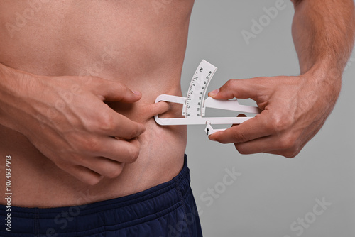 Man measuring body fat with caliper on grey background, closeup photo