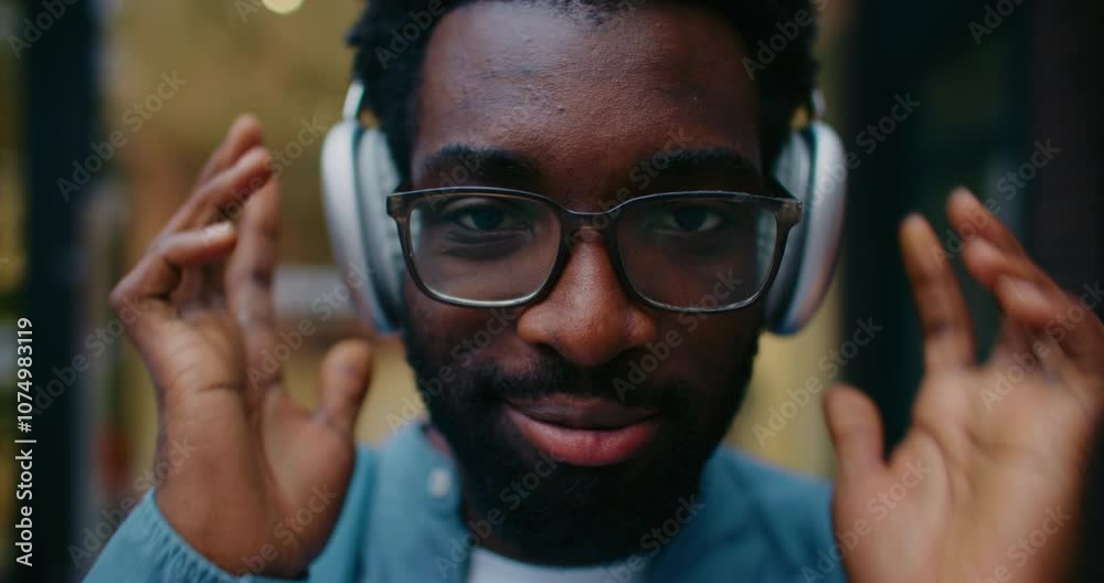Very close facial view of African American man placing headphones on his ears. Pressing button on side. Enjoying listening to music. Nodding head to rhythm while looking directly at camera.