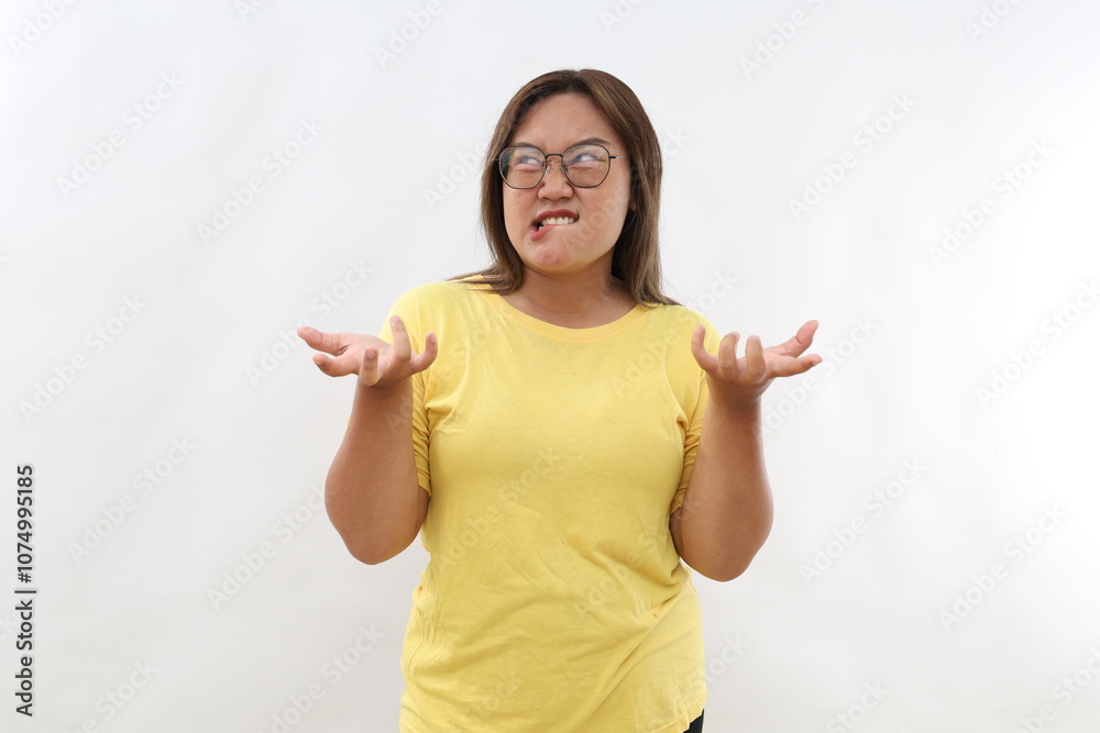 Irritated Asian woman with dark hair bites lips and gestures angrily being annoyed with someone expresses negative emotions wears t-shirt isolated over white background. People aggression anger. Irritated Asian woman with dark hair bites lips and gestures angrily being annoyed with someone expresses negative emotions wears t-shirt isolated over white background. People aggression anger.