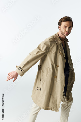 Φωτογραφία Stylish dandy in a trench coat striking a pose against a minimalist backdrop