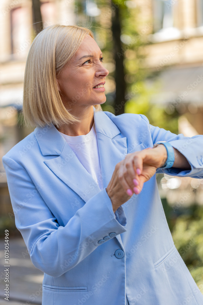Fototapeta premium Serious sad businesswoman standing outdoors looking around waiting for business meeting impatient woman dissatisfied looks at wristwatch, checks time on watch annoyed by being late lateness concept.