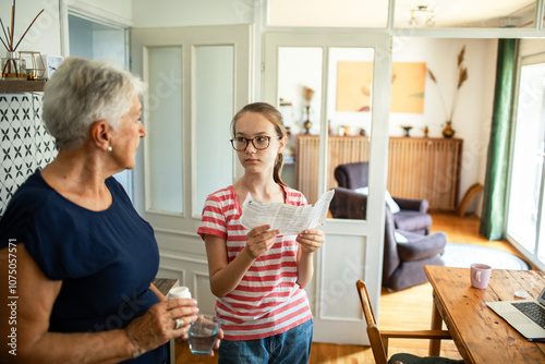 Granddaughter helping grandmother with bills on kitchen table with laptop photo