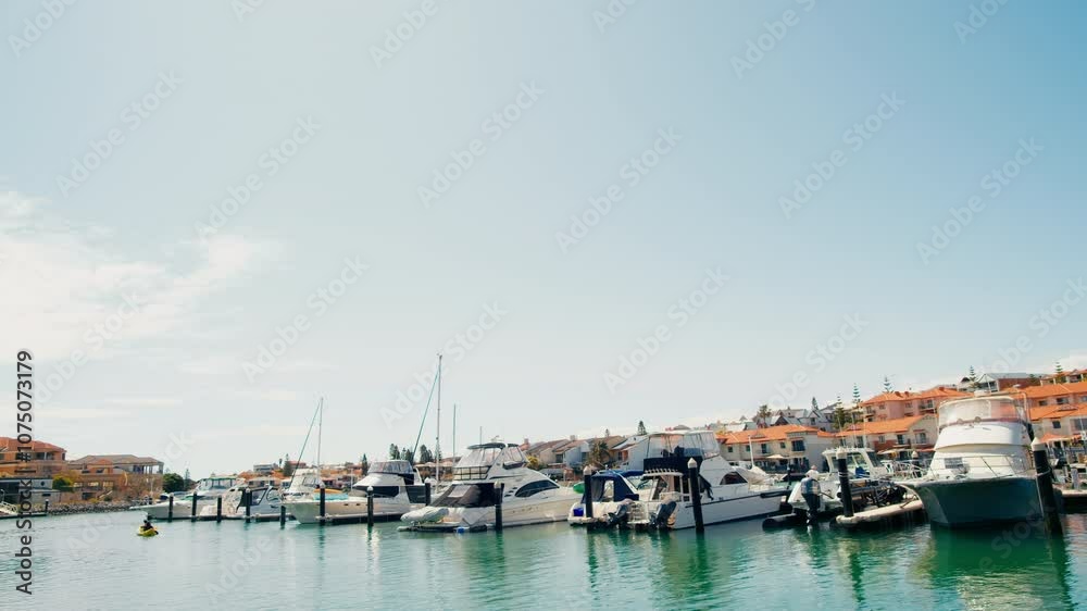 Several boats are docked in a marina on a sunny day. The boats are all white with blue accents