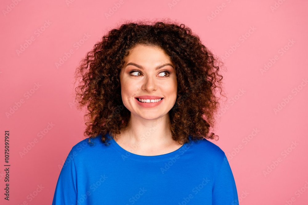 Fototapeta premium Young woman with curly hairstyle in blue sweatshirt against a pink background, looking joyful and confident