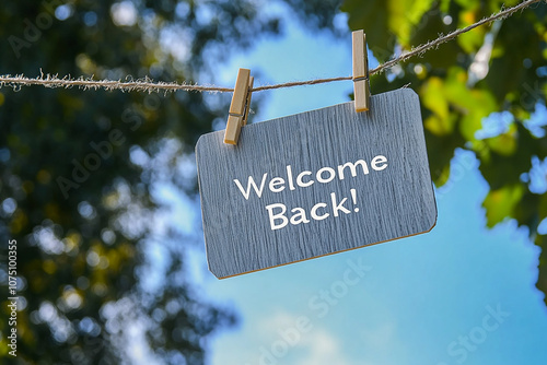 A simple, elegant sign with the words Welcome Back! hanging on a clothesline against a blue sky background