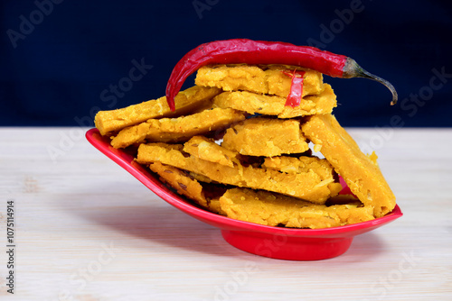 Side view of Gujarati Kathiyawadi Spicy Dhokali Sabji with a red chilli sitting atop a bowl. The stunning black backdrop highlights the red dish's distinctive features photo