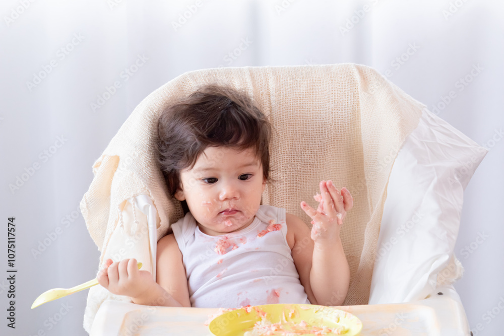 Adorable happy little toddler daughter get celebrate of birthday party at home with parent. Cute infant girl gets hungry Enjoy eating by using hand. baby girl holding a spoon try to feed herself Adorable happy little toddler daughter get celebrate of birthday party at home with parent. Cute infant girl gets hungry Enjoy eating by using hand. baby girl holding a spoon try to feed herself