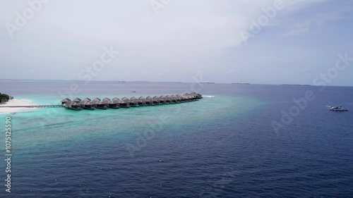 Top view of the bungalow on the water. Maldives. Luxury villas near the green island. The view from the drone. Turquoise water, beautiful reef. The rays of the sun on the surface of the ocean. Waves