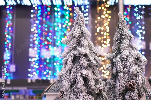 Snow-covered artificial Christmas trees in Scandinavian style on the background of colorful glowing garlands in the store before the Christmas sale photo