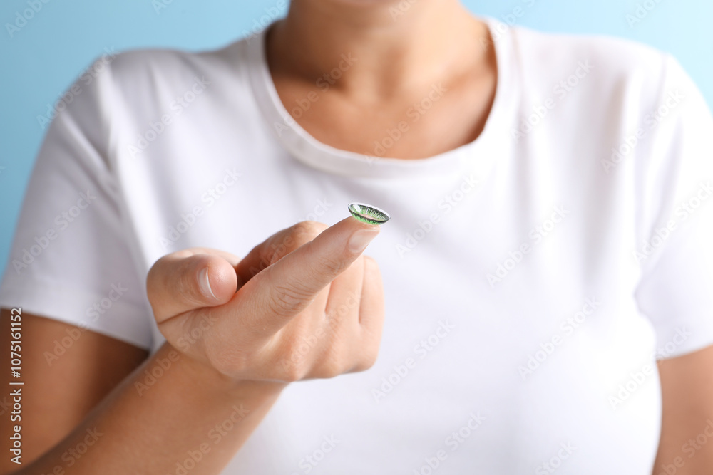 Woman holding color contact lens on light blue background, closeup Woman holding color contact lens on light blue background, closeup