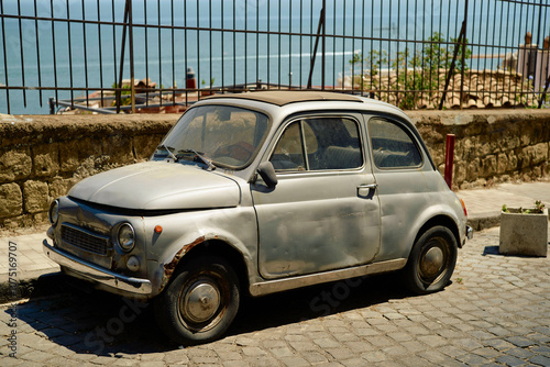 Vintage small car parked by a seaside fence under a clear sky, Naples, Italy