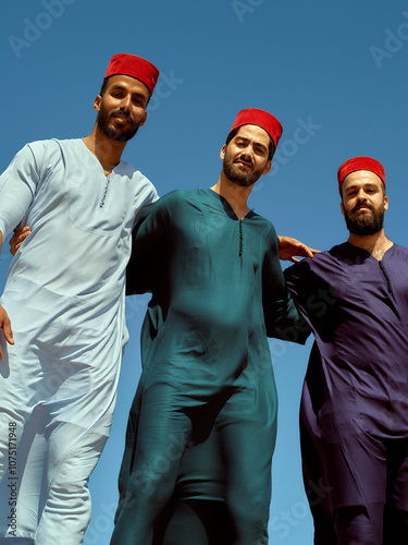 Three men in traditional attire and red fez hats posing against a clear blue sky, Morocco photo