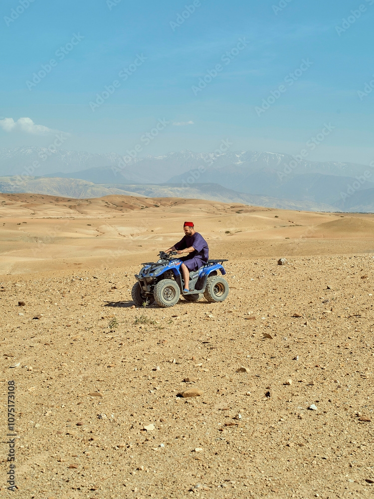Person riding an ATV through a barren desert landscape with mountains in the background on a clear day, Morocco Person riding an ATV through a barren desert landscape with mountains in the background on a clear day, Morocco
