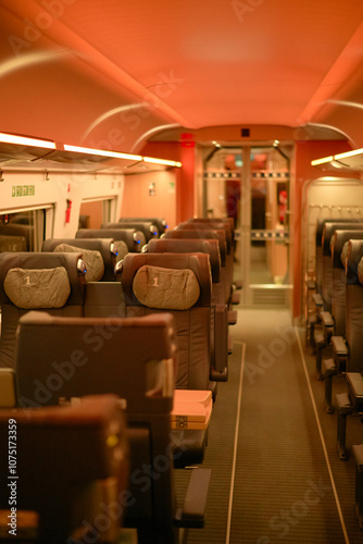 Empty train carriage interior with rows of seats illuminated by warm overhead lighting at night. photo