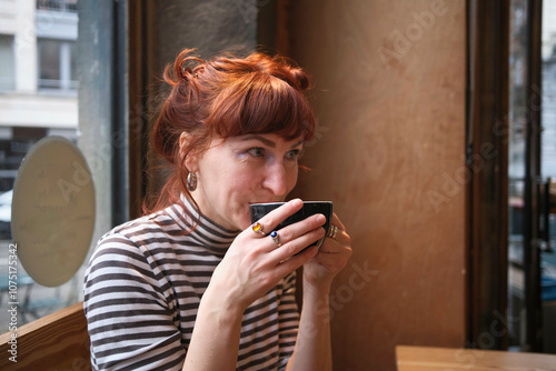 A woman with red hair sipping coffee in a cafe, looking away from the camera with a thoughtful expression, Brussels, Belgium