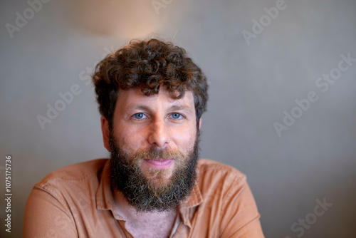 Smiling bearded man with curly hair posing for a portrait against a blurred background. photo