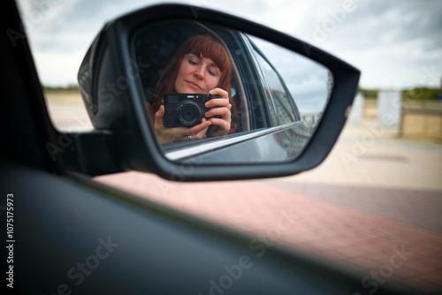 Woman takes a photo of herself in a car side mirror with a camera. photo