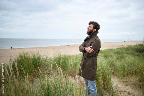 Smiling man with a beard enjoying a breezy day at the beach with tall grass in the foreground and cloudy skies above, Belgium photo