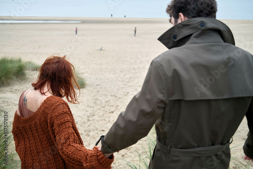 Couple holding hands walking towards a beach with others in the distance and overcast skies, Belgium photo