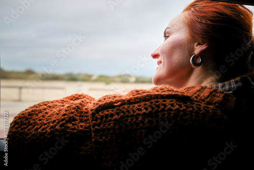 Side view of a woman with red hair looking out of a window, wearing a brown knitted sweater and hoop earrings, Belgium photo