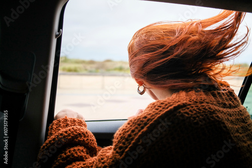 Woman with red hair in a brown sweater looks out the car window on a windy day, Belgium photo