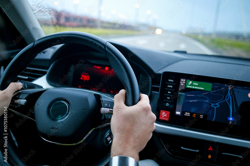 Close-up of a driver's hands on a steering wheel with a dashboard and navigation screen in focus. Close-up of a driver's hands on a steering wheel with a dashboard and navigation screen in focus.