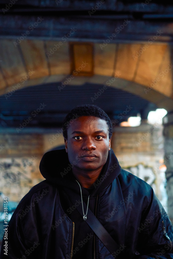 Confident young man in a black jacket standing under a bridge, Berlin, Germany Confident young man in a black jacket standing under a bridge, Berlin, Germany