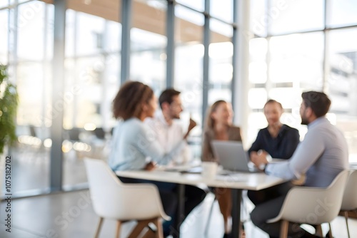 A softly blurred scene of business people gathered around a table in a modern office.