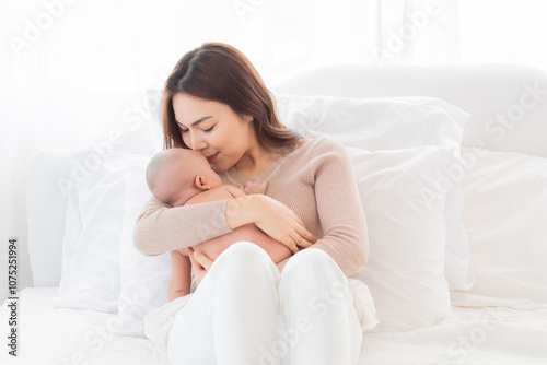 Young cheerful and beautiful Asian mom sleeping baby in arm, mother and newborn bonding relationship. Mother holding adorable healthcare nurturing. woman tenderly cuddles infant with love and care