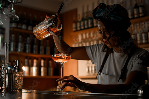 Female bartender prepared a cocktail in a mixing glass and strained it through a strainer into a glass