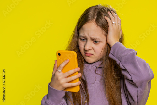 Upset sad preteen child girl kid use smartphone typing browsing, play game, loses, surprised by sudden lottery results, bad fortune, loss, fail, unlucky news. Sad children on yellow background indoors photo